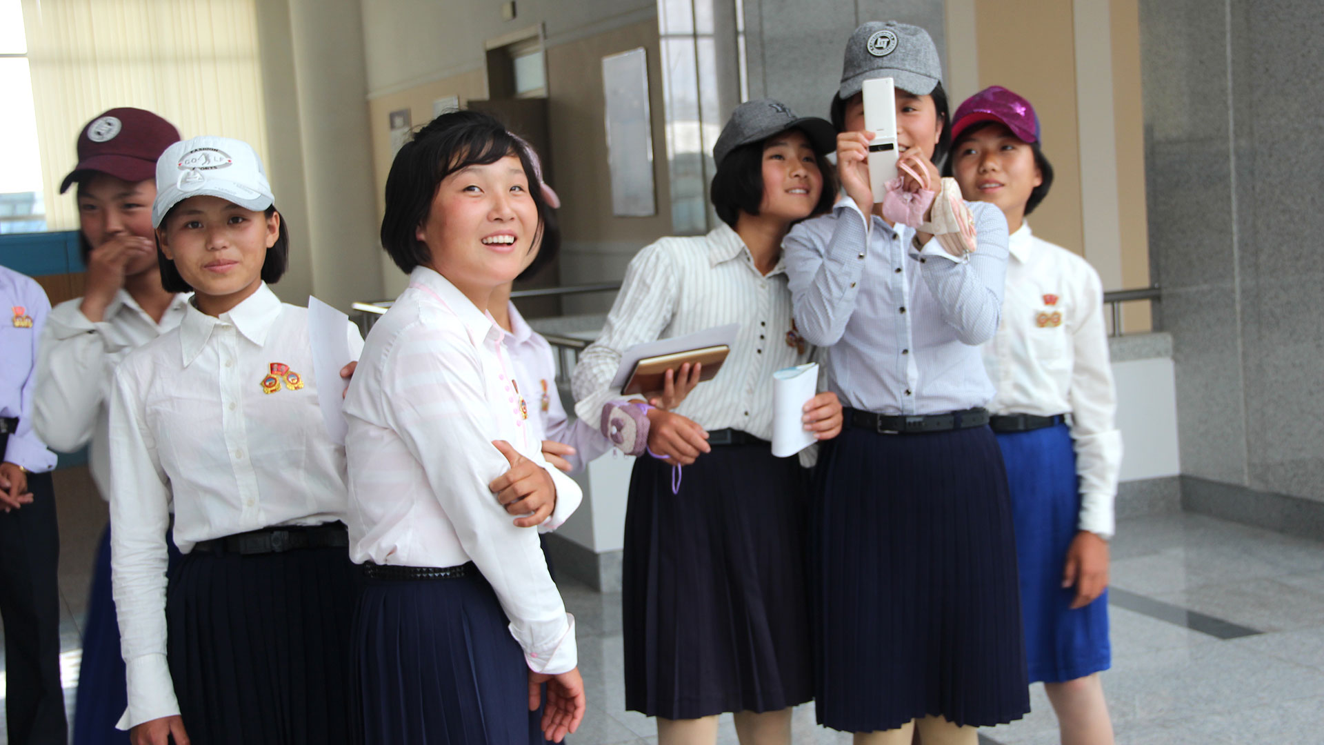 Estudiantes de secundario de Pyongyang, identificadas con prendedores oficiales, toman fotos a los extranjeros con un teléfono celular. (Foto: Florencia Grieco – @flowergrieco)