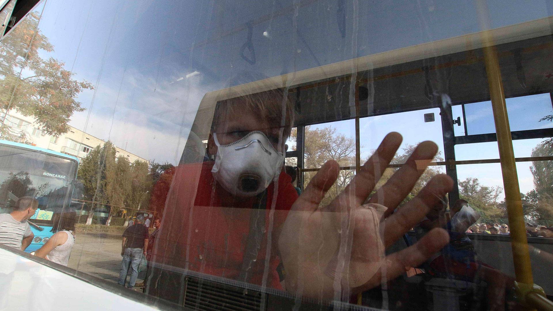 Niños con barbijos saludan desde un ómnibus que los alejará de una zona afectada por el escape (Reuters)